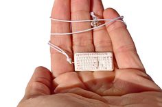 a hand holding a tiny white keyboard in it's palm with string attached to it