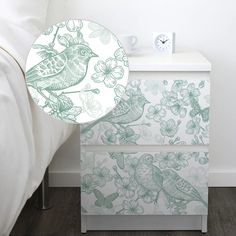 a white nightstand with green birds and flowers on it next to a night stand that has an alarm clock