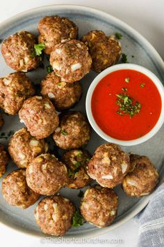 some meatballs are on a plate with a small bowl of tomato sauce next to it