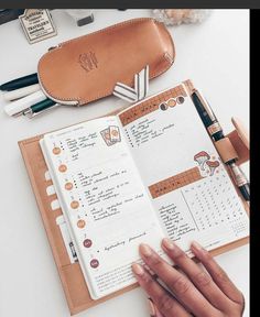 a person's hand holding an open planner next to a pen and pencils