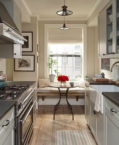 a kitchen with white cabinets and gray counter tops next to a small dining table in front of a window