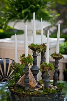 a table with candles, moss and rocks on it in front of an outdoor dining area