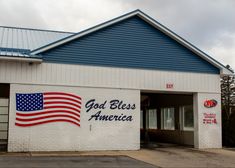 an american flag painted on the side of a white brick building that says god bless america