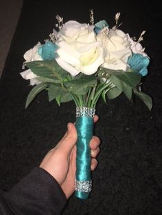 a person holding a bouquet of white and blue roses in a vase with green ribbon