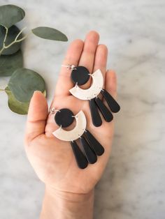 two black and white earrings are held in someone's hand next to a plant