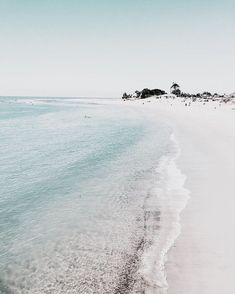 an empty beach with white sand and blue water