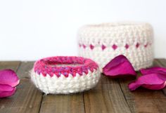 two crocheted baskets sitting on top of a wooden table next to pink flowers