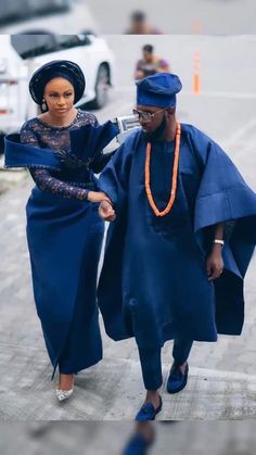 two women walking down the street in blue dresses and headgear, one wearing an orange beaded necklace