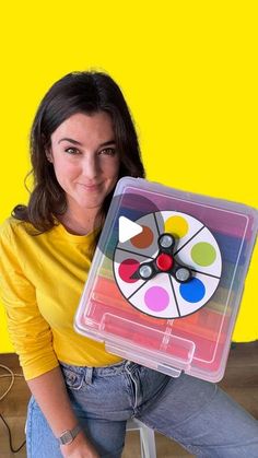 a woman sitting on a stool holding a plastic box with a video game in it