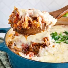 a spoon full of meat and cheese being lifted out of a blue casserole dish