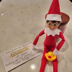 an elf is sitting on the counter next to a cup with a rubber duck in it