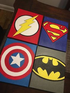 four canvases with superhero logos on them are sitting on a table in front of a wall