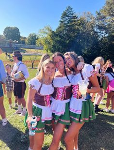 two women in costume hugging each other on the grass at an outdoor event with people standing around