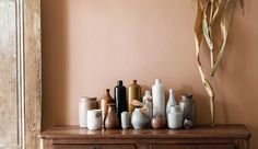 an assortment of vases and jars sit on a dresser in front of a dried plant