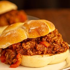 a sloppy joe sandwich sitting on top of a white plate next to other buns