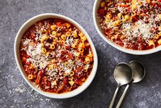 two bowls filled with pasta and cheese on top of a table next to spoons