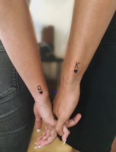 two people holding hands with small tattoos on their arms and the other hand behind them