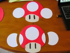 paper cut out of mario mushroom sitting on top of a wooden table next to a laptop computer