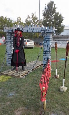 a man dressed in black and red standing next to a brick structure with chains on it