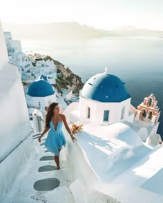 a woman in a blue dress is walking up some steps to the water and buildings