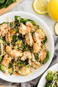 a white bowl filled with broccoli and cauliflower next to lemon wedges