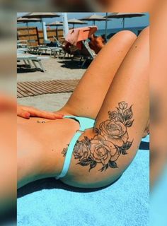 a woman laying on top of a towel next to a swimming pool with roses tattooed on her side