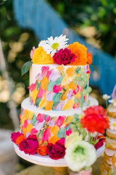 a multi - tiered cake with colorful flowers on it is sitting next to other desserts