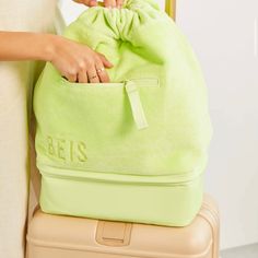 a woman holding onto a green bag on top of a piece of luggage