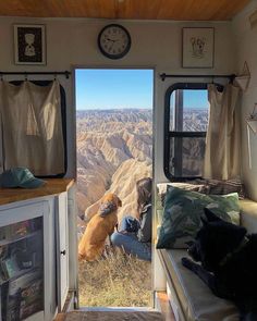 a dog sitting in the doorway of a camper looking out at mountains and valleys