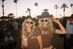 two young women wearing cowboy hats and sunglasses at a music festival with palm trees in the background