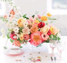 a vase filled with lots of colorful flowers on top of a white table next to silverware