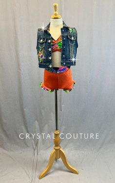 a mannequin wearing a denim jacket and colorful skirt on a wooden stand against a white backdrop