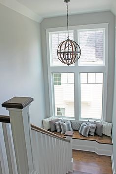 a window seat in the corner of a room next to a stair case with pillows on it