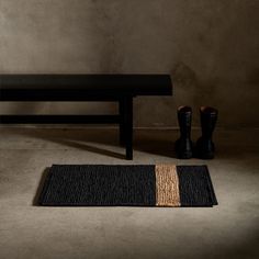 a black bench and rug in front of a table with two boots on the floor