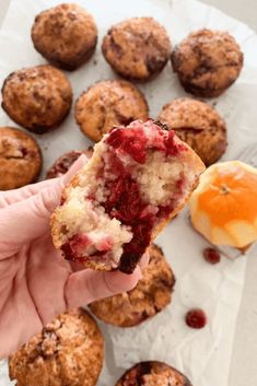 a hand holding up a muffin with cranberry toppings and an orange in the background