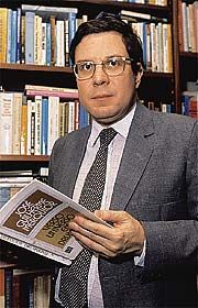 a man in a suit and tie is holding a book while standing in front of a bookshelf