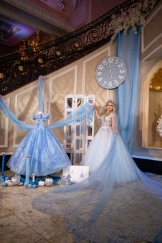 a woman in a blue dress standing next to two dresses and a clock on the wall