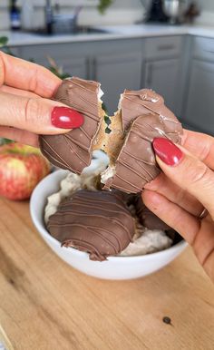 two hands holding pieces of chocolate covered dessert in front of an apple on a kitchen counter