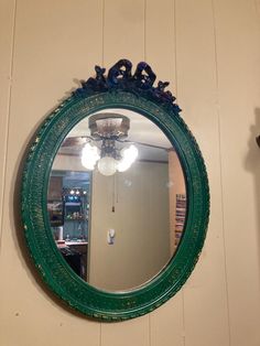 a green mirror hanging on the wall above a light fixture and a blue bird figurine