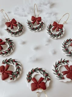 twelve christmas wreath ornaments with red bows and green leaves hanging from them on a white surface