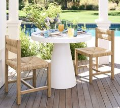 two chairs and a table on a wooden deck next to a pool with water in the background