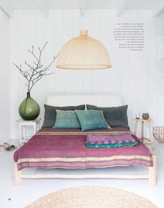 a bed with pillows and blankets in a room next to a lamp on the wall