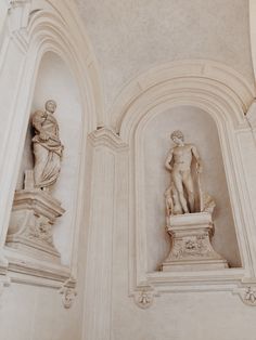 two statues in the middle of a room with white walls and arches on either side