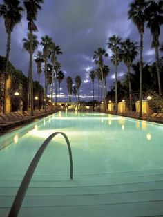 an empty swimming pool surrounded by palm trees at night with lights shining on the water