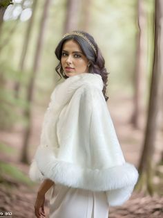 a woman wearing a white fur stole in the woods with her hands on her hips