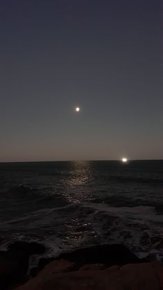 the sun is setting over the ocean with two moon's in the sky above it