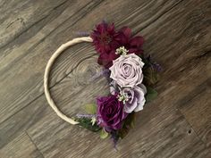 a wreath with purple flowers and greenery sits on a wood floor in front of a wooden wall