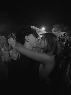 two people kissing each other in front of a crowd at an outdoor music festival on a dark night