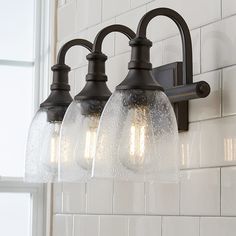 three light bathroom fixture with clear glass shades on the bottom and black metal fixtures above it