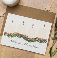 a card with three candles on it sitting next to a candle holder and some greenery